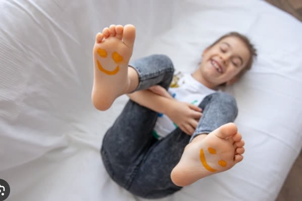 Criança sorrindo com carinhas desenhadas na sola dos pés